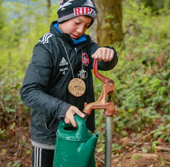 student filling watering can from outdoor pump